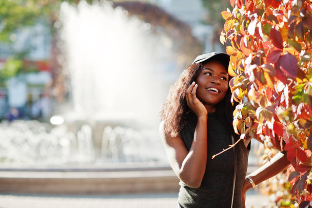 Stylish african american girl in cap posed at sunny autumn day against red leaves. Africa model woman. - Valokuva, kuva