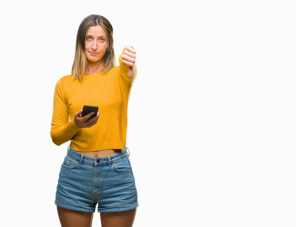 Молодая красивая женщина отправляет сообщение с помощью смартфона на изолированном фоне с сердитым лицом, негативный знак, показывающий неприязнь с опущенными пальцами, концепция отказа
 - Фото, изображение