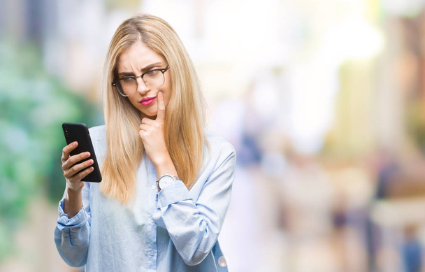 Young beautiful blonde business woman using smartphone over isolated background serious face thinking about question, very confused idea - Zdjęcie, obraz