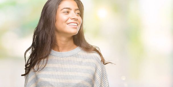 Young beautiful arab woman wearing winter sweater over isolated background looking away to side with smile on face, natural expression. Laughing confident. - Photo, Image