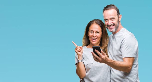 Middle age hispanic couple texting message on smartphone ver isolated background very happy pointing with hand and finger to the side - Φωτογραφία, εικόνα