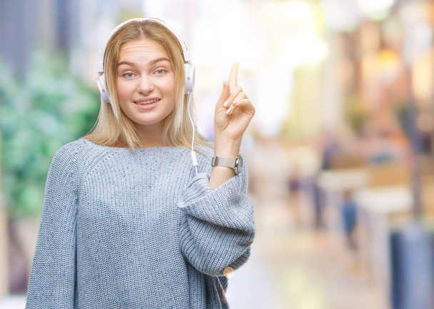 Genç kafkas kadın başarılı fikirle izole arka plan işaret parmağı üzerinde kulaklık giyen müzik dinlemek. Çıktıktan ve mutlu. Bir numara. - Fotoğraf, Görsel