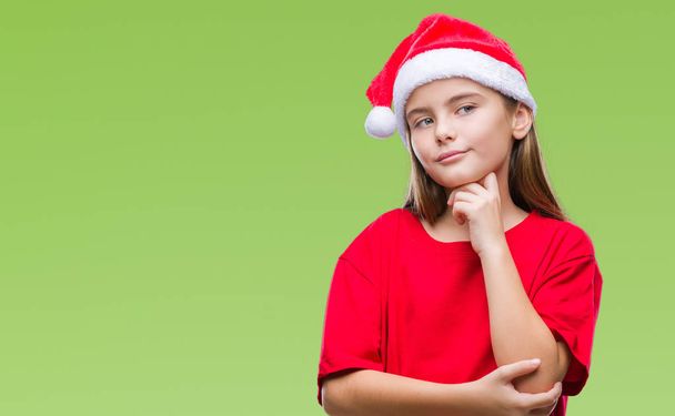 Young beautiful girl wearing christmas hat over isolated background with hand on chin thinking about question, pensive expression. Smiling with thoughtful face. Doubt concept. - Photo, image