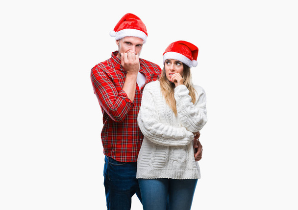 Młoda para w miłości w sobie Boże Narodzenie kapelusz na białym tle patrząc zestresowany i zdenerwowany z rąk na ustach gryzienie paznokci. Problem lęku. - Zdjęcie, obraz