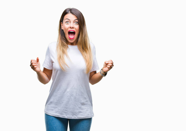 Young beautiful woman casual white t-shirt over isolated background celebrating surprised and amazed for success with arms raised and open eyes. Winner concept. - Foto, Imagen