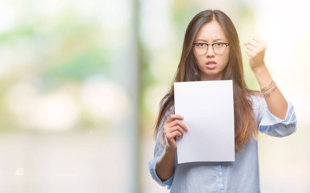 Молодая азиатская женщина держит чистую бумагу на изолированном фоне раздраженный и разочарованный кричать от гнева, сумасшедший и кричать с поднятой рукой, гнев концепции
 - Фото, изображение