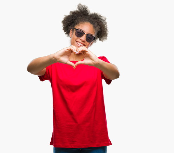 Молодих афро Американку носити сонцезахисні окуляри над ізольованих фону, посміхаючись в любові, показуючи серце символ і форма руками. Романтичної концепції. - Фото, зображення