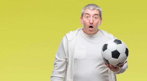 Bello uomo anziano che tiene palla da calcio su sfondo isolato spaventato in stato di shock con una faccia a sorpresa, spaventato ed eccitato con espressione di paura
 - Foto, immagini