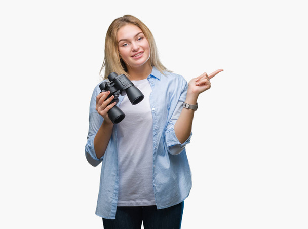 Nuori valkoihoinen nainen pitää kiikarit yli eristetty tausta erittäin onnellinen osoittaa käsin ja sormella sivulle
 - Valokuva, kuva