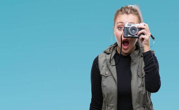 Jeune femme blonde prenant des photos à l'aide d'une caméra vintage sur fond isolé effrayé en état de choc avec un visage surprise, effrayé et excité par l'expression de la peur
 - Photo, image