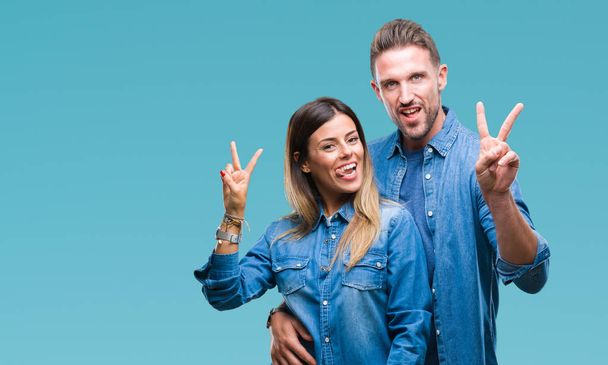 Young couple in love over isolated background smiling with happy face winking at the camera doing victory sign. Number two. - Fotoğraf, Görsel