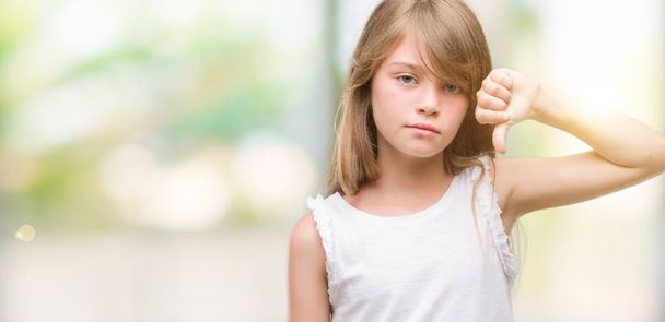 Fiatal szőke kisgyermek dühös arccal, negatív előjellel mutatja nem szeretik a hüvelykujját lefelé, elutasítás koncepció - Fotó, kép