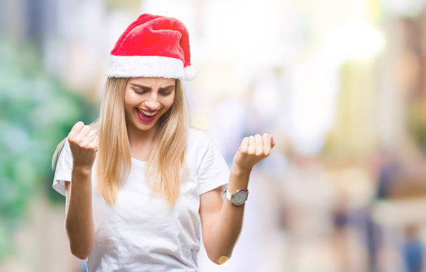 非常に幸せと興奮して腕を上げると、笑みを浮かべて、成功のために叫んで勝者ジェスチャーを行う分離の背景に若い金髪美人クリスマス帽子。お祝いのコンセプト. - 写真・画像