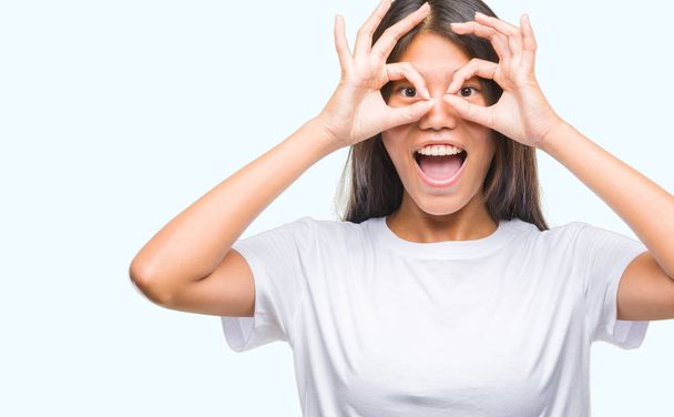 Young asian woman over isolated background doing ok gesture like binoculars sticking tongue out, eyes looking through fingers. Crazy expression. - Foto, Bild