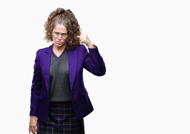 Young brunette student girl wearing school uniform and glasses over isolated background angry and mad raising fist frustrated and furious while shouting with anger. Rage and aggressive concept. - Photo, Image