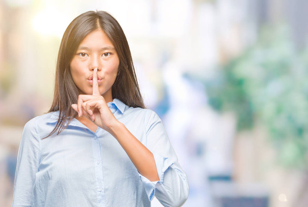 Молода азіатська бізнес-леді над ізольованим тлом просить бути тихою з пальцем на губах. Тиша і таємна концепція
. - Фото, зображення
