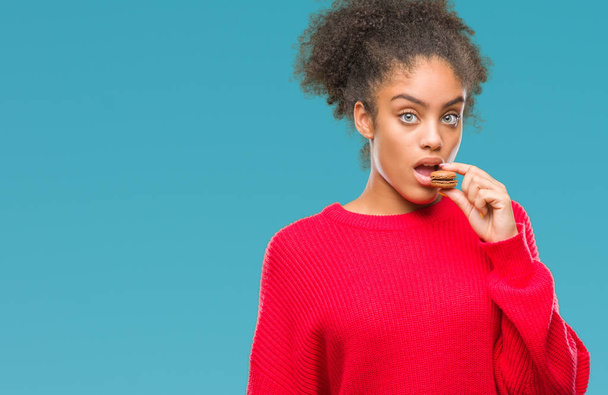 junge Afroamerikanerin isst Schokoladenmacaron über isoliertem Hintergrund mit selbstbewusstem Gesichtsausdruck und ernstem Denken - Foto, Bild