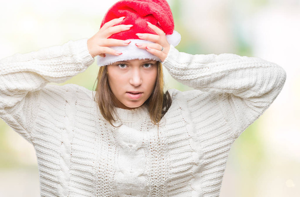 Νέοι όμορφη καυκάσιος γυναίκα φοράει καπέλο Χριστουγέννων πέρα από το απομονωμένο υπόβαθρο που υποφέρουν από πονοκέφαλο, απελπισμένος και τόνισε επειδή τον πόνο και την ημικρανία. Τα χέρια στο κεφάλι. - Φωτογραφία, εικόνα
