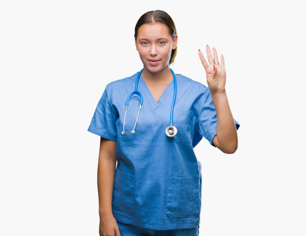 Молода біла жінка-лікар в медичній формі над ізольованим фоном, показуючи і вказуючи пальцями номер чотири, посміхаючись впевнено і щасливо
. - Фото, зображення