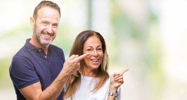 Middle age hispanic casual couple over isolated background with a big smile on face, pointing with hand and finger to the side looking at the camera. - Zdjęcie, obraz