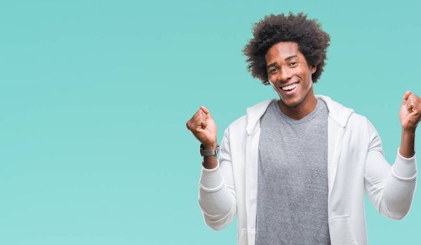 Homem afro-americano vestindo camisola sobre fundo isolado comemorando surpreso e surpreso pelo sucesso com os braços levantados e olhos abertos. Conceito de vencedor
. - Foto, Imagem