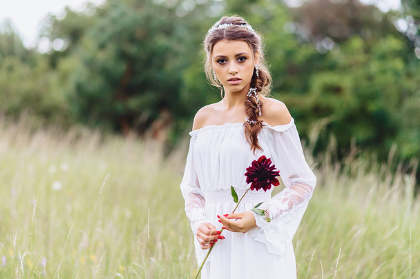 joven bonita chica con flor en sus manos en vestidor ligero caminar en el césped cerca de verde bosque de verano
 - Foto, imagen