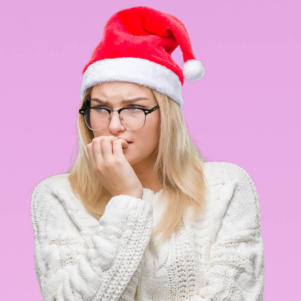 Καυκάσιος γυναίκα φοράει καπέλο Χριστουγέννων πέρα από το απομονωμένο υπόβαθρο ψάχνει αγχωμένοι και νευρικοί με τα χέρια στο στόμα δάγκωμα νύχια. Πρόβλημα του άγχους. - Φωτογραφία, εικόνα