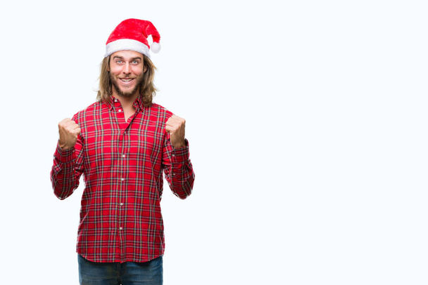 Nuori komea mies pitkät hiukset yllään joulupukki hattu yli eristetty tausta juhlii yllättynyt ja hämmästynyt menestystä kädet esille ja avoimet silmät. Voittajan käsite
. - Valokuva, kuva