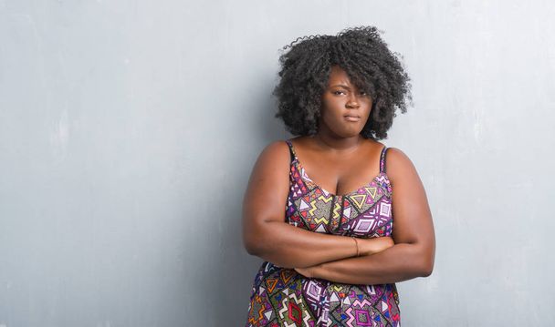 Mladá africká americká žena přes zeď šedá grunge nosí barevné šaty skeptik a nervózní, nesouhlasným výrazem na tváři s překřížením rukou. Negativní osoba. - Fotografie, Obrázek
