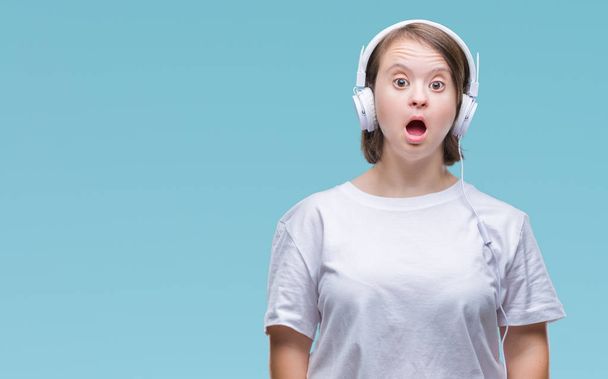 Young adult woman with down syndrome wearing headphones over isolated background afraid and shocked with surprise expression, fear and excited face. - Foto, imagen