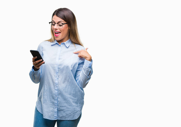 Jonge mooie zakelijke vrouw SMS bericht via smartphone over geïsoleerde achtergrond met verrassing gezicht wijzende vinger naar zichzelf - Foto, afbeelding