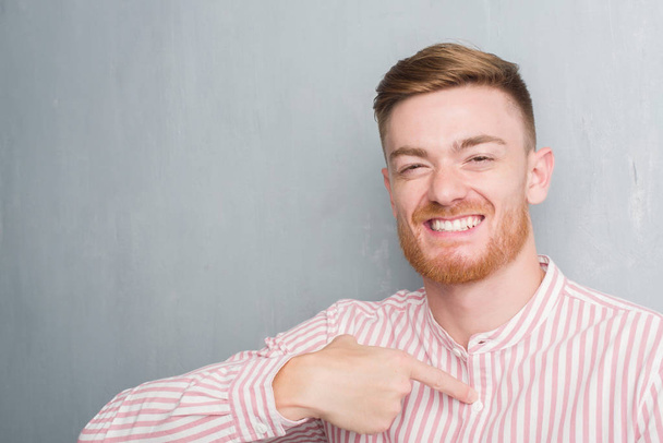 Young redhead man over grey grunge wall with surprise face pointing finger to himself - Photo, Image