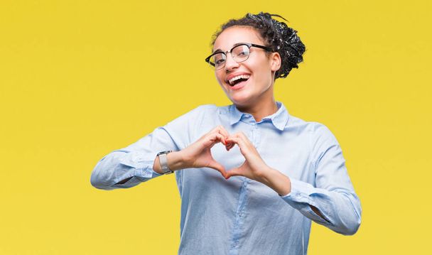 Jonge gevlochten haar Afrikaanse Amerikaanse bedrijfsleven meisje met bril op geïsoleerde achtergrond glimlachend in liefde met hartsymbool en vorm met de handen. Romantische concept. - Foto, afbeelding