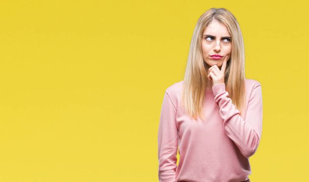 Young beautiful blonde woman wearing pink winter sweater over isolated background with hand on chin thinking about question, pensive expression. Smiling with thoughtful face. Doubt concept. - Фото, изображение