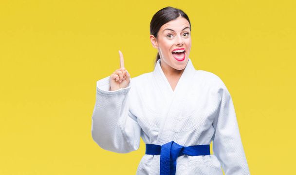 Mujer hermosa joven que usa uniforme de kimono de karate sobre un fondo aislado apuntando con el dedo hacia arriba con una idea exitosa. Salido y feliz. Número uno.
. - Foto, imagen