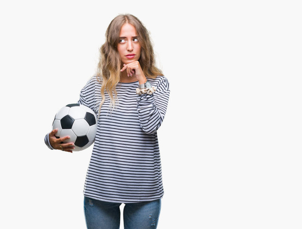 İzole arka plan ciddi bir yüz düşünme hakkında soru, çok karışık bir fikir üzerinde futbol futbol topu tutan genç güzel sarışın kadın - Fotoğraf, Görsel