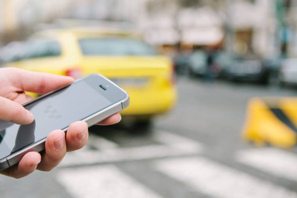 Yakın çekim, bir mans el bir telefon onun elinde tutan ve bir mobil uygulaması kullanarak bir taksi çağırma. - Fotoğraf, Görsel