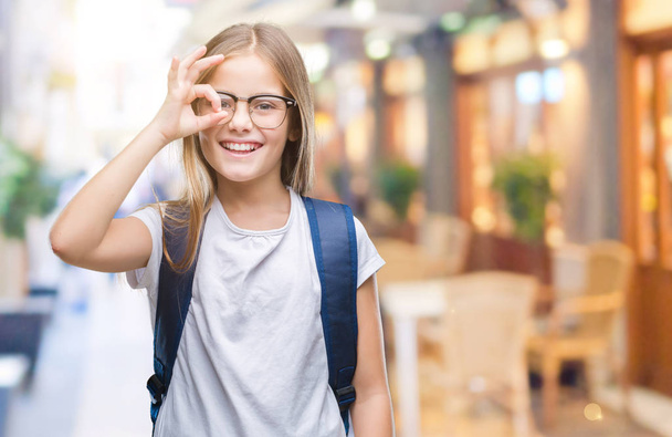 Young beautiful smart student girl wearing backpack over isolated background doing ok gesture with hand smiling, eye looking through fingers with happy face. - Фото, зображення