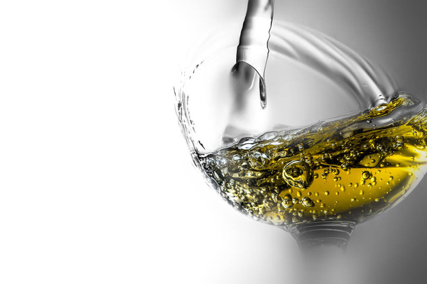 Stream of white wine pouring into a glass, white wine splash close-up on a grey background. Black and white photo with color of wine and beautiful fog around - Zdjęcie, obraz