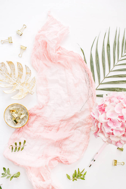 Elegante composición con flores de hortensia rosa ramo, hoja de palma tropical, manta pastel, placa de hoja de monstera y accesorios sobre fondo blanco. Piso tendido, vista superior
. - Foto, Imagen
