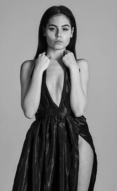 Sexy decollete concept. Woman in elegant black evening dress with decollete, grey background. Attractive girl wears expensive fashionable evening dress with erotic slit. Lady, sexy girl in dress - Φωτογραφία, εικόνα
