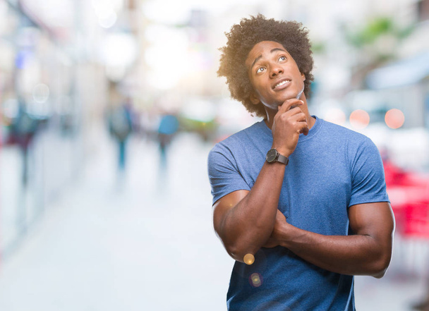 Afro-amerikai ember feletti elszigetelt háttér kézzel a chin gondolkodás kérdés, töprengő kifejezés. Mosolygós, figyelmes arccal. Kétség koncepció. - Fotó, kép