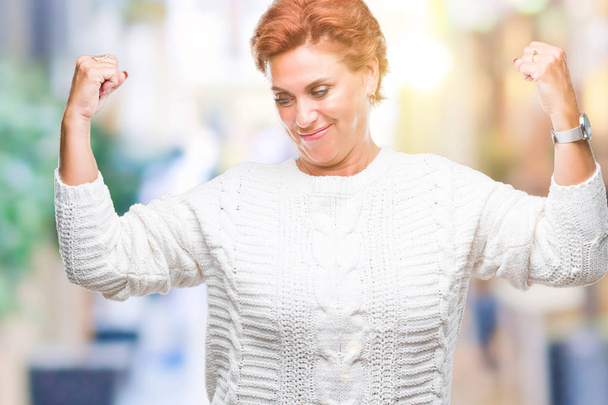 Виступаюча старша біла руда жінка в зимовому светрі над ізольованим тлом, показуючи м'язи рук, що посміхаються, пишаючись. Концепція фітнесу
. - Фото, зображення