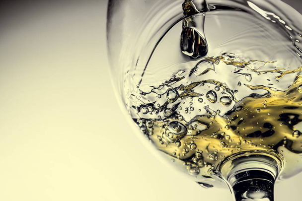 Stream of white wine pouring into a glass, white wine splash close-up on a grey background. Black and white photo with color of wine. Vintage, grunge, old, retro style. - Foto, imagen