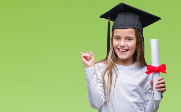 Молода красива дівчина в шапці випускника тримає ступінь над ізольованим тлом дуже щасливий вказуючи рукою і пальцем на бік
 - Фото, зображення