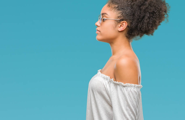 Giovane donna afro americana che indossa occhiali da sole su sfondo isolato cercando di lato, posa profilo relax con viso naturale con sorriso fiducioso
. - Foto, immagini