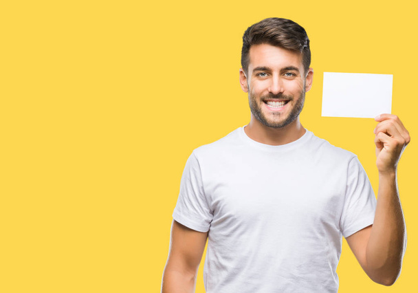 Young handsome man holding blank card over isolated background with a happy face standing and smiling with a confident smile showing teeth - Foto, Imagen