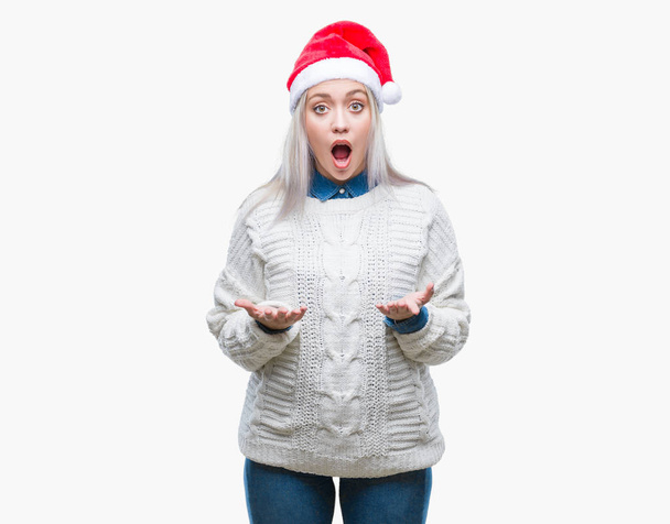 恐れ、驚きの表現、恐怖と興奮した顔でショックを受けて孤立した背景にクリスマス帽子身に着けている若いブロンドの女性. - 写真・画像