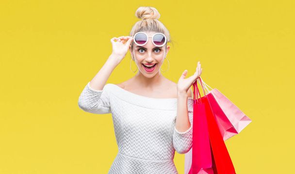 Young beautiful blonde woman holding shopping bags over isolated background scared in shock with a surprise face, afraid and excited with fear expression - Foto, imagen