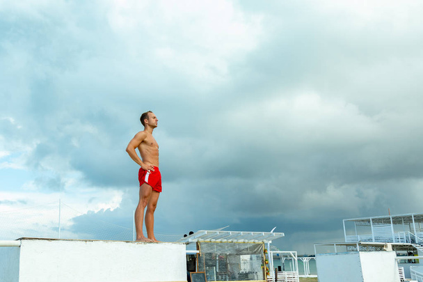 Handsome Athlete Shirtless Young Man stands on a rock against the sky - Photo, Image